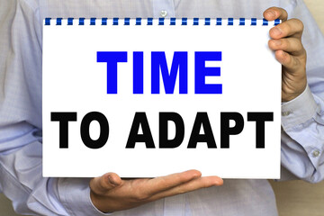 The businessman shows a sheet with the text OF TIME TO ADAPT on a white background. Business concept