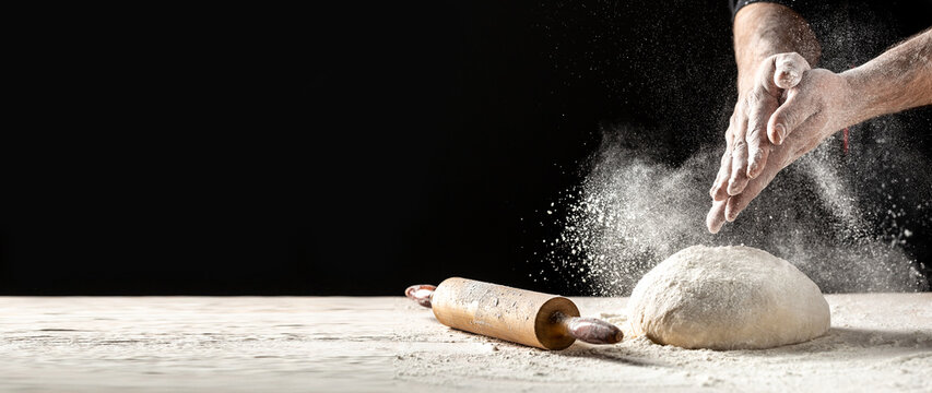 White flour flying into air as pastry chef in white suit slams ball dough on white powder covered table. concept of nature, Italy, food, diet and bio