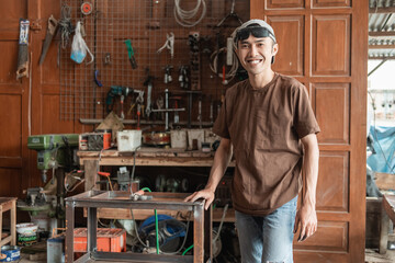 Male welder smiles at the camera holding a metal rack against the welding workshop background