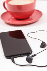 Smartphone with connected headphones and coffee with milk. Relaxation time with music. White background