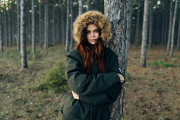 Fototapeta na wymiar A woman stands near a tree in a warm jacket with a hood nature lifestyle