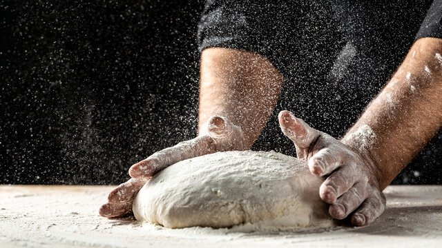 chef in a professional kitchen prepares the dough with flour, Beautiful and strong men's hands knead the dough from which they will then make bread, pasta or pizza