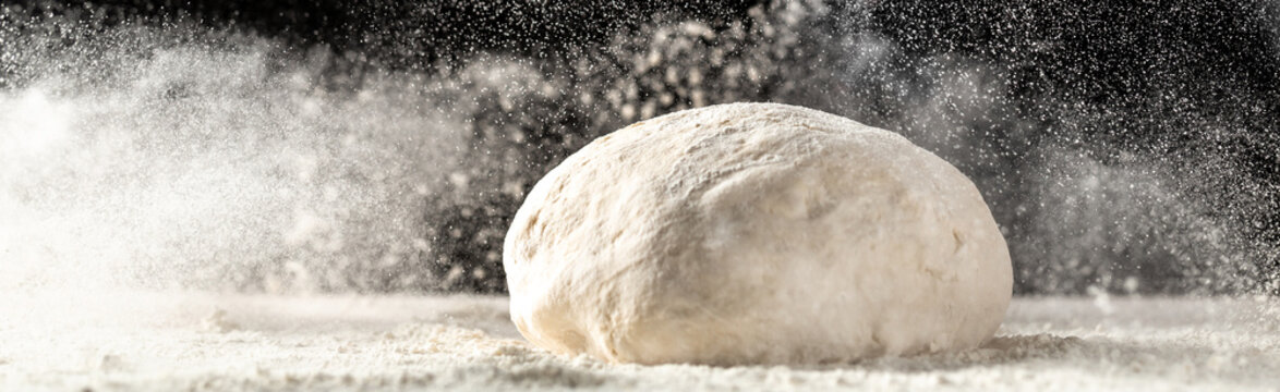 yeast dough for bread or pizza on a floured surface, with flour splash. Cooking bread. Kneading the Dough. Long banner format.