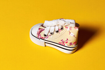 Baby girl modern sneakers decorated with beautiful print. Isolated on the yellow background. Sale, discount and advertisement backdrop