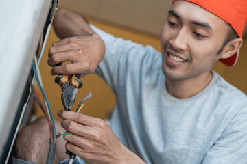 close up of an asian electronics worker using pliers to fix a washing machine cable that broke an...