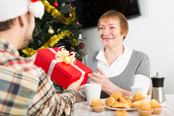 Elderly mother and son gives gifts to each other for Christmas at festive table