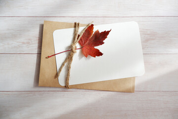 A Colorful maple leaf with black card on white wooden background. Autumn greeting.