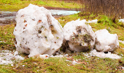 Snowman melted with the arrival of spring on a background of green grass. Destroyed, dirty snowman lies on the ground. Holiday of Christmas and New Year is over. Remains of a snowman.