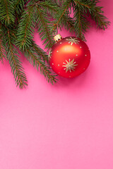 Natural pine branch with red christmas decoration on pink background. Flat lay, top view.