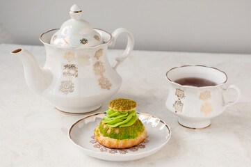 Shu cake with pistachio cream and a white tea set on the table