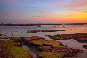 Obraz premium Seascape. Beach with rocks and stones. Low tide. Pink sunset. Slow shutter speed. Soft focus. Melasti beach, Bali, Indonesia