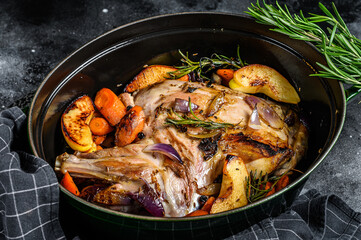 Baked whole lamb shoulder leg in a baking dish.  Black background. Top view