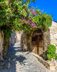 Fototapeta na wymiar Traditional architecture with narrow stone street and a colorfull bougainvillea in the medieval castle of Monemvasia, Lakonia, Peloponnese, Greece.