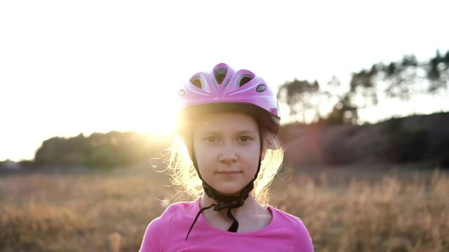 A little girl in a Bicycle helmet puts on a pink medical mask at sunset before Cycling.