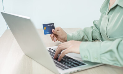 The businesswoman's hand is holding a credit card and using a laptop for online shopping and internet payment in the office