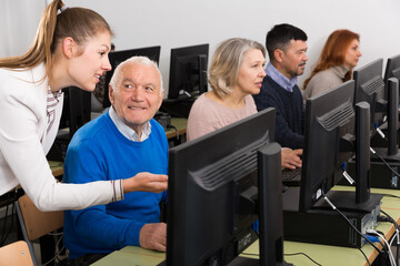 Computer lessons for adults. Young woman instructing smiling senior man in computer skills