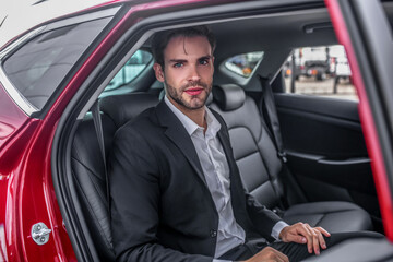 Fototapeta na wymiar Brown-haired male sitting at backseat of red car