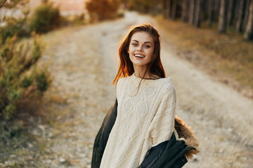 Cheerful pretty woman in a white sweater with a jacket outdoors the road