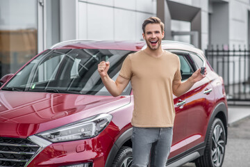 Excited young male screaming with joy in front of red car