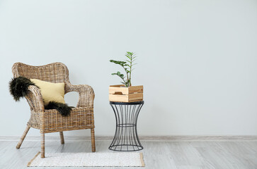 Stylish armchair with pillow and table with houseplant near light wall in room