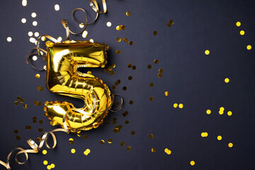 Gold foil balloon number and digit five 5. Birthday greeting card. Anniversary celebration event. Banner. Copy space. Stylish golden numeral, light bokeh, glitter, black background. Numerical digit.