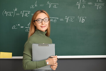 Mature maths teacher near blackboard in classroom