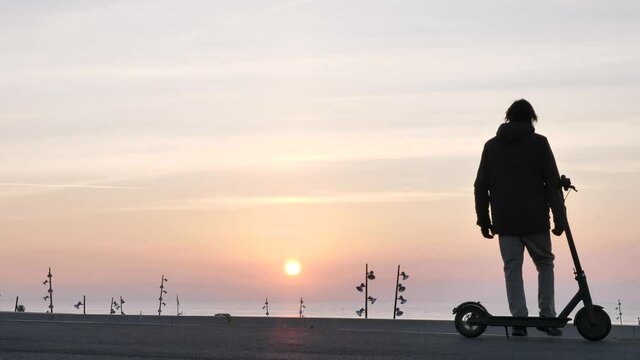 Man on e scooter stops and takes a moment to admire the beach sunrise