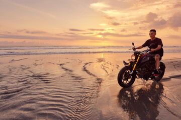 Fototapeta na wymiar Man And Motorcycle On Ocean Beach At Beautiful Tropical Sunset. Handsome Biker On Motorbike On Sandy Coast In Bali, Indonesia.