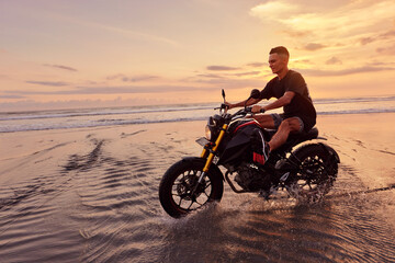 Obraz na płótnie Canvas Man And Motorcycle On Ocean Beach At Beautiful Tropical Sunset. Handsome Biker On Motorbike On Sandy Coast In Bali, Indonesia.