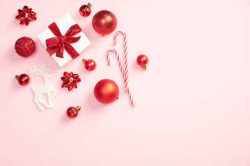 White gift box with ribbon bow and red Christmas decorations on pastel pink background. Xmas composition. Minimal style.