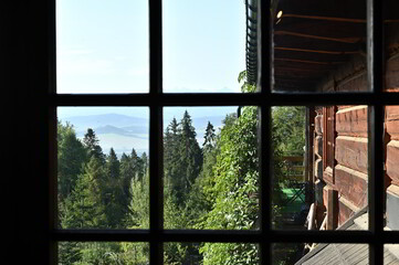 Beautiful view on green trees forest, blue sky and mountains through a wooden window frame of an...