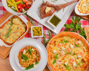 Flat lay shot of delicious italian pizza, tomahawk steak with pasta and casserole over red plaid tablecloth.