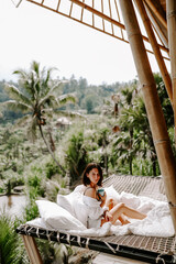 Young travel blogger and influencer girl relaxing in a bamboo house hotel in Bali surrounded by rice terraces and palm trees