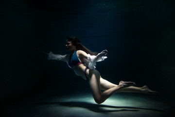 Fototapeta na wymiar Slender pretty young woman brunette in bathing suit and white blouse in dark pond, illuminated by moonlight. Elegant female underwater. Concept of beauty, tenderness and striving for ideal. Copy space