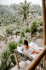 Young travel blogger and influencer girl relaxing in a bamboo house hotel in Bali surrounded by...