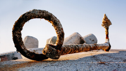 Rusty anchor ring and chain on concrete pier with blurred rocks in background
