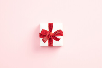 Gift box with red ribbon bow on pink background. Christmas present, valentine day surprise, birthday concept.