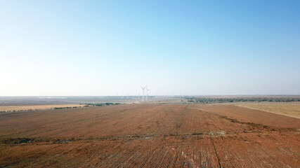 Windmills near the field. Top view from a drone. Blue sky, light shroud, windmills turn, green energy is generated. Alternative energy, clean land. Yellow plants, and a desert. Industrial farm.