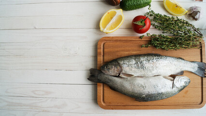 Two rainbow trout on a board, with herbs , ready for cooking.