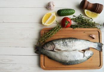 Two rainbow trout on a board, with herbs , ready for cooking.