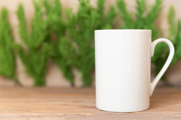 Mockup - White cup on Christmas tree branches background. Coffee or tea mug for your design
