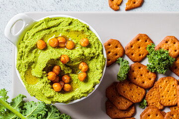 Green kale hummus in white bowl with crackers. Vegan chickpea dip, top view. Healthy vegetarian food concept.