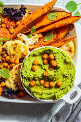 Vegetarian food concept. Baked vegetables with green kale hummus, light background. Summer healthy food.