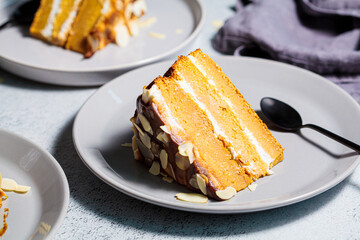 Piece of vegan cake on gray plate. Homemade carrot cake with white cream, caramel and nuts.