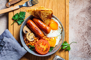 English breakfast with sausages, beans, fried eggs, toast, mushrooms and tomato in frying pan, dark background. English breakfast concept.
