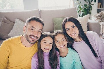 Photo of full family four people two little kids cuddle white shiny smile wear colorful sweater in living room indoors