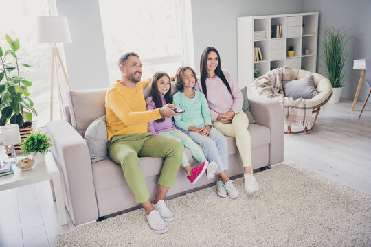 Photo of full family four people sit couch dad hold remote control wear colorful sweater in living room indoors