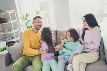 Photo of full big family four people sit sofa tickling having fun wear colorful pullover pants in...