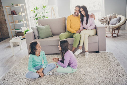 Photo of full family four members sit sofa carpet two small children conversation wear colorful pullover pants in living room indoors