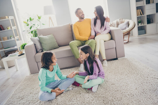Photo of full family four members sit couch floor two little children have chat wear colorful jumper trousers in living room indoors